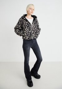 Fleece hoodie med leopardmönster och svarta detaljer, dragkedja fram och fickor, parat med mörka bootcut-jeans och platåskor.