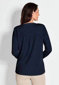 Marineblaues Langarmshirt mit entspannter Passform, rundem Halsausschnitt und Passen-Detail auf der Rückseite. Weicher Stoff, minimalistisches Design, kombiniert mit beigen Hosen.
