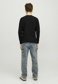 Čierna dlhá rukávová košeľa skombinovaná s oversized svetlomodrými cargo džínsy s viacerými vreckami, nosená s hnedými sandálmi.