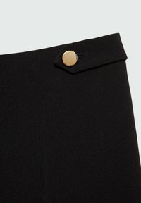 Zwarte op maat gemaakte broek met een gladde textuur, een opvallende gouden knop in de taille en een strakke, gestructureerde uitstraling met minimale naden.