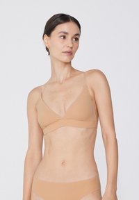 Nackter Triangel-Bralette aus weichem Stoff mit verstellbaren Trägern. Nahtloses Design mit glatter Textur und minimalistischem Stil.