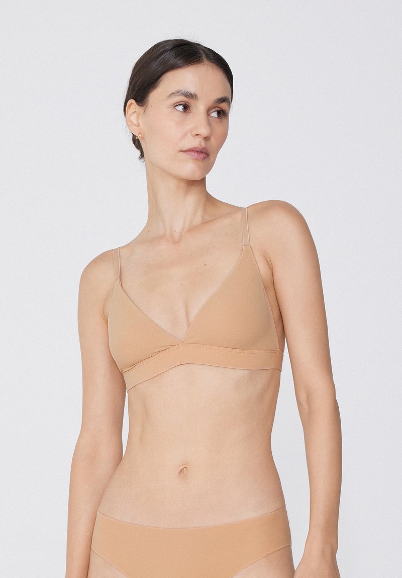 Nackter Triangel-Bralette aus weichem Stoff mit verstellbaren Trägern. Nahtloses Design mit glatter Textur und minimalistischem Stil.