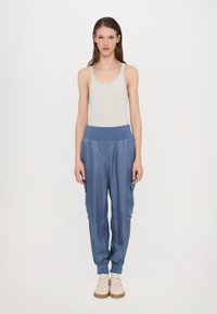 Lichtgrijze tanktop en losse, blauwe satijnen cargobroek met elastische tailleband. Witte sneakers met vetersluiting.