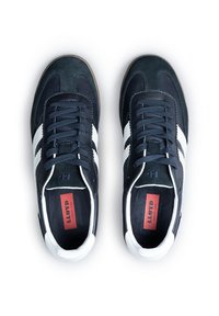 Ciemnoniebieskie zamszowe sneakersy z białymi paskami, z płaskimi sznurowadłami, gumową podeszwą i czerwoną wkładką z logo widoczną od wewnętrznej strony.