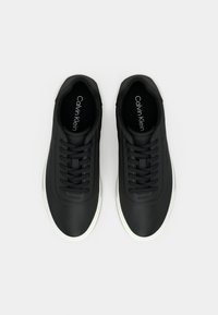 Ζεύγος μαύρα αθλητικά παπούτσια Calvin Klein με λευκές σόλες, απεικονιζόμενα από πάνω, δεμένα με κορδόνια σε απλό ανοιχτό φόντο.