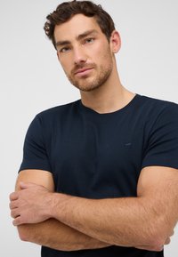 Granatowa koszulka z krótkim rękawem, wykonana z bawełny, z okrągłym dekoltem i małym haftowanym logo na piersi. Gładka tekstura.