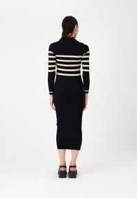 Črna rebrasta midi obleka z dolgimi rokavi, ki ima vodoravno smetanasto črtasto zasnovo čez prsa in zgornje roke. Čevlji so z debelim peto.