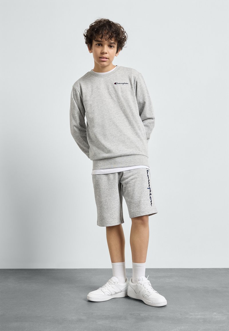 Felpa grigia e pantaloni corti in tessuto morbido, con un piccolo logo. Completati da sneakers bianche e calzini alla caviglia. Design semplice e casual.