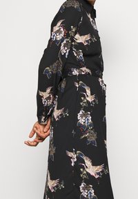 Abito nero floreale con maniche lunghe, colletto e cintura annodata in vita. Il motivo include uccelli e design floreali in colori tenui.