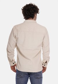 Camicia in corduroy beige con maniche lunghe e dettagli in plastica nera sui polsini, caratterizzata da un design a yoke e un tessuto a coste testurizzato.