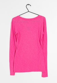 Langärmliges Oberteil in leuchtendem Pink, aus einem weichen, strukturierten Stoff mit einem U-Boot-Ausschnitt und einer lockeren Passform. Hängt an einem schwarzen Haken.