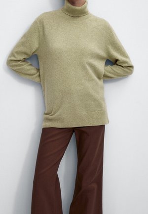 Vaaleanvihreä pörröinen turtleneck-neule, joka on pehmeää neulosta, yhdistettynä leveälahkeisiin ruskeisiin housuihin. Neuleessa on rento istuvuus ja ribbireunat.