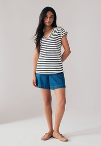 Randig svartvit v-ringad t-shirt, jeansshorts och beiga ballerinaskor. Kortärmad, avslappnad passform, strukturerat tyg med sidofickor.