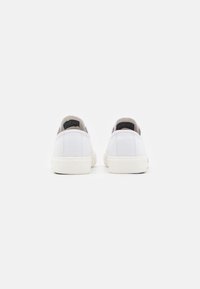 Sneakers bianchi in tela con design a bassa struttura, caratterizzati da una suola in gomma testurizzata e una linguetta sul tallone nera. Stile semplice e minimalista.