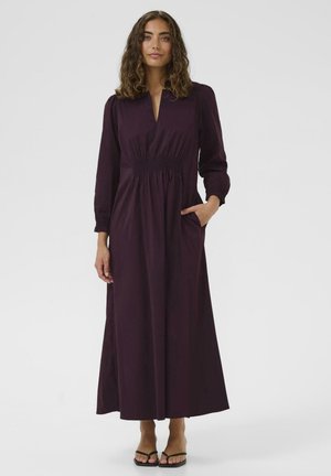 Long, deep purple dress with a v-neck, gathered waistline, long sleeves, and side pockets. Smooth fabric with a flowing design.