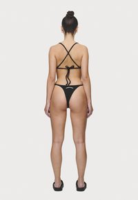 Svart bikini med trekantet topp med kryssede stropper og knyting bak, kombinert med en minimal truse.