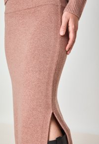 Jupe tricotée rose avec fentes latérales, mettant en avant une texture douce et un design ajusté. La taille est côtelée pour un détail supplémentaire.