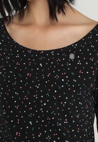 Svart topp med rundad halsringning och korta ärmar, prydd med ett spritt mönster av rosa, blå och vita former.