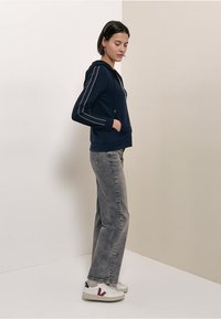 Sweat à capuche bleu marine avec des détails en passepoil blanc, poche kangourou et capuche à cordon, associé à un jean gris à jambes droites et des baskets blanches.