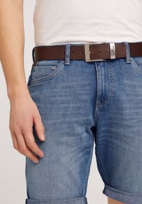 Shorts en denim de couleur bleu clair avec une coupe décontractée, présentant des ourlets retroussés, une ceinture en cuir marron avec une boucle en métal argenté, et des poches latérales.