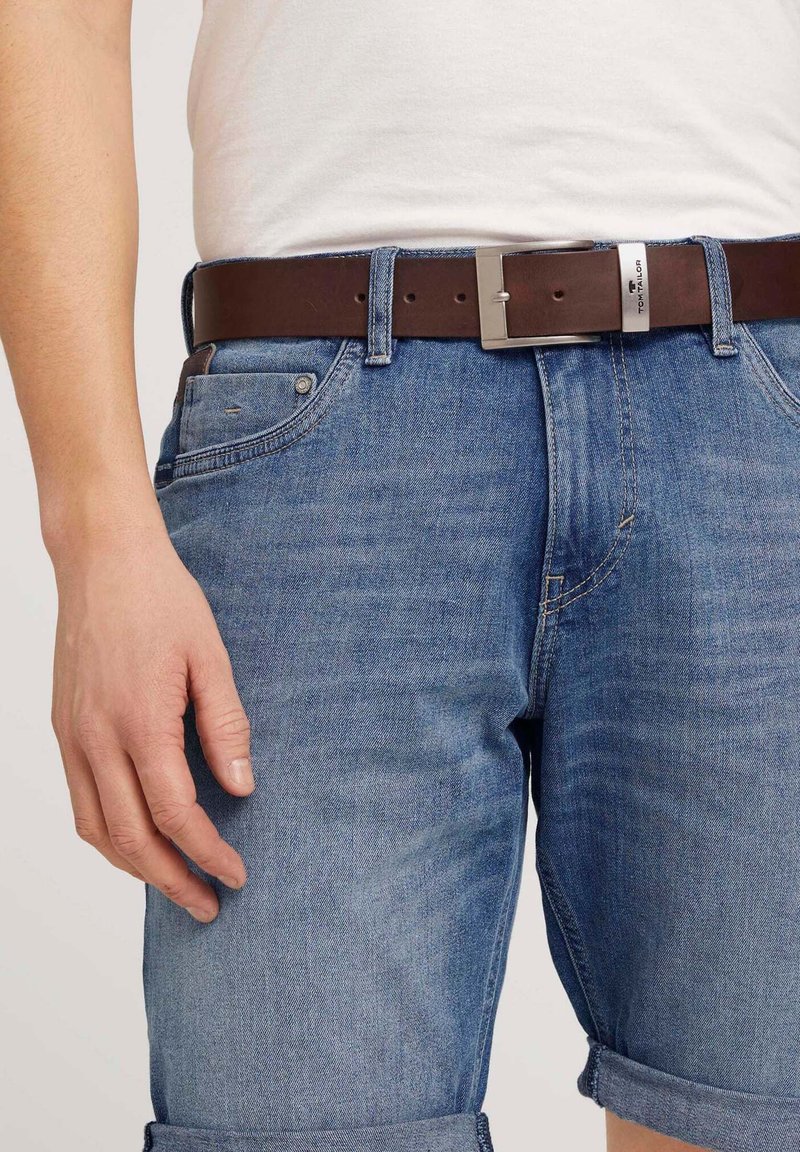 Shorts en denim de couleur bleu clair avec une coupe décontractée, présentant des ourlets retroussés, une ceinture en cuir marron avec une boucle en métal argenté, et des poches latérales.