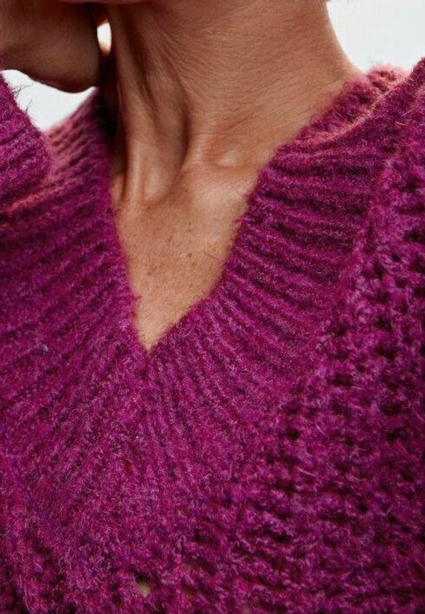 Gros plan d'une personne portant un pull en maille texturée violet avec un col en V, montrant son cou et une partie de sa mâchoire.