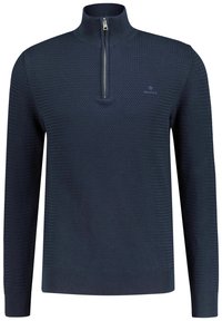 Pull en tricot bleu marine avec un col montant et une fermeture éclair argentée, présentant un motif texturé ainsi que des poignets et un ourlet côtelés. Logo GANT sur la poitrine.
