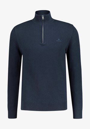 Pull en tricot bleu marine avec un col montant et une fermeture éclair argentée, présentant un motif texturé ainsi que des poignets et un ourlet côtelés. Logo GANT sur la poitrine.