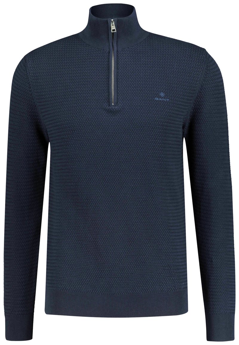 Pull en tricot bleu marine avec un col montant et une fermeture éclair argentée, présentant un motif texturé ainsi que des poignets et un ourlet côtelés. Logo GANT sur la poitrine.