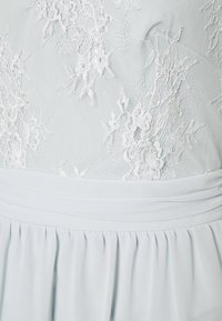 Vestido azul claro com um corpete de renda transparente com padrões florais, uma cintura de tecido suave e uma saia plissada.