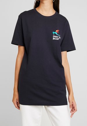 Kvinde iført en sort T-shirt med korte ærmer med et farverigt grafik og teksten "Exhale the Bullshit" på venstre bryst.