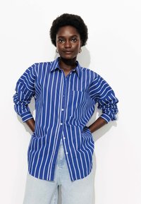 Chemise à rayures bleu et blanche avec un col, poche poitrine et manches longues, fabriquée en tissu léger.