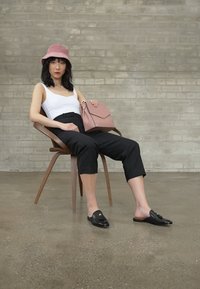 Hvit tank topp, svarte avkortede bukser, svarte loafers med dekorasjon, rosa håndveske, rosa bøttehatt, sittende på trekappe mot murvegg.