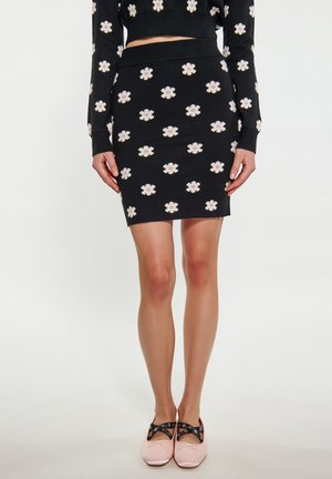 Fustă tricotată neagră cu model floral în alb și violet. Însoțită de pantofi roz cu curele negre și ochiuri decorative.