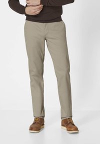 Beige Baumwollhosen mit schmaler Passform und geradem Bein, ausgestattet mit frontalen Taschen und dezenten Nähten, getragen mit braunen Schnürstiefeln.