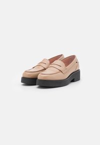Mocassins en cuir verni beige avec semelles compensées noires épaisses, style sans lacets et coutures décoratives sur fond blanc.