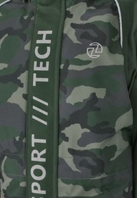 Camouflage jack in verschillende tinten groen met een gladde textuur. Beschikt over een verticale band met "TECH" en "SPORT" in witte letters.