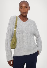 Gray knitted sweater with a V-neck, cable knit design, and loose fit. Styled with an olive green shoulder bag featuring a gold accent.