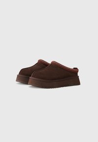 Chaussures brunes à enfiler en daim, ornées d'un accent tissé rouge et vert texturé sur le collier et dotées d'une semelle extérieure épaisse et robuste.