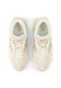 Scarpe da ginnastica beige con texture in rete e camoscio, dotate di lacci bianchi, colletto imbottito e un logo di marca riconoscibile sulla linguetta.
