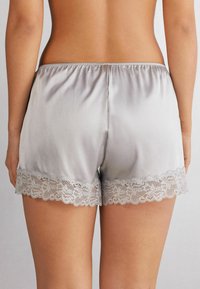 Silkeslena grå shorts med elastisk midja och delikat spetskant. Mjuk textur och lös passform, lämpliga för hemmabruk eller sömn.