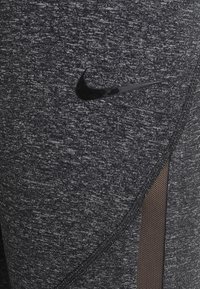 Leggings sportivi neri con un tessuto testurizzato, dotati di un'apertura con pannello in rete e un logo Nike nero sul lato sinistro superiore.