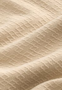 Beige textured fabric with a geometric pattern, featuring a smooth weave and subtle sheen, draping softly in folds.