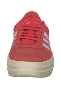 Crvene suède tenisice s okruglim vrhom, bijelim trostrukim dizajnom na bočnim stranama, uparenim crvenim vezicama i debelim kremastim potplatima.