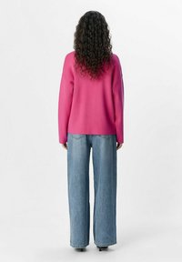Jersey de punto sobredimensionado en fucsia con mangas largas combinado con unos pantalones vaqueros de mezclilla azul de pierna ancha, que presentan un ajuste relajado y un diseño minimalista.