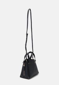 Sac à main en cuir noir avec une longue bandoulière réglable, deux poignées supérieures et des détails de fermeture éclair dorés sur un fond uni.