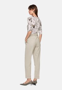 Light gray tailored trousers with a high waist and rolled cuffs, paired with a black and white patterned top, and gray heeled shoes.