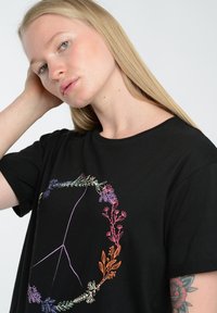 Czarny bawełniany t-shirt z nadrukiem kwiatowego symbolu pokoju w żywych kolorach. Krótkie rękawy i okrągły dekolt oraz luźny krój.
