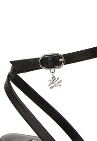 Sort lædersandalrem med oval sølvspænde og vedhæng med "h" i kursiv. Glat tekstur med minimalistisk design.