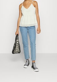Top peplum en dentelle blanche avec des bretelles fines, jeans en denim bleu clair avec des pois blancs, sac fourre-tout en mesh noir et baskets montantes noires.